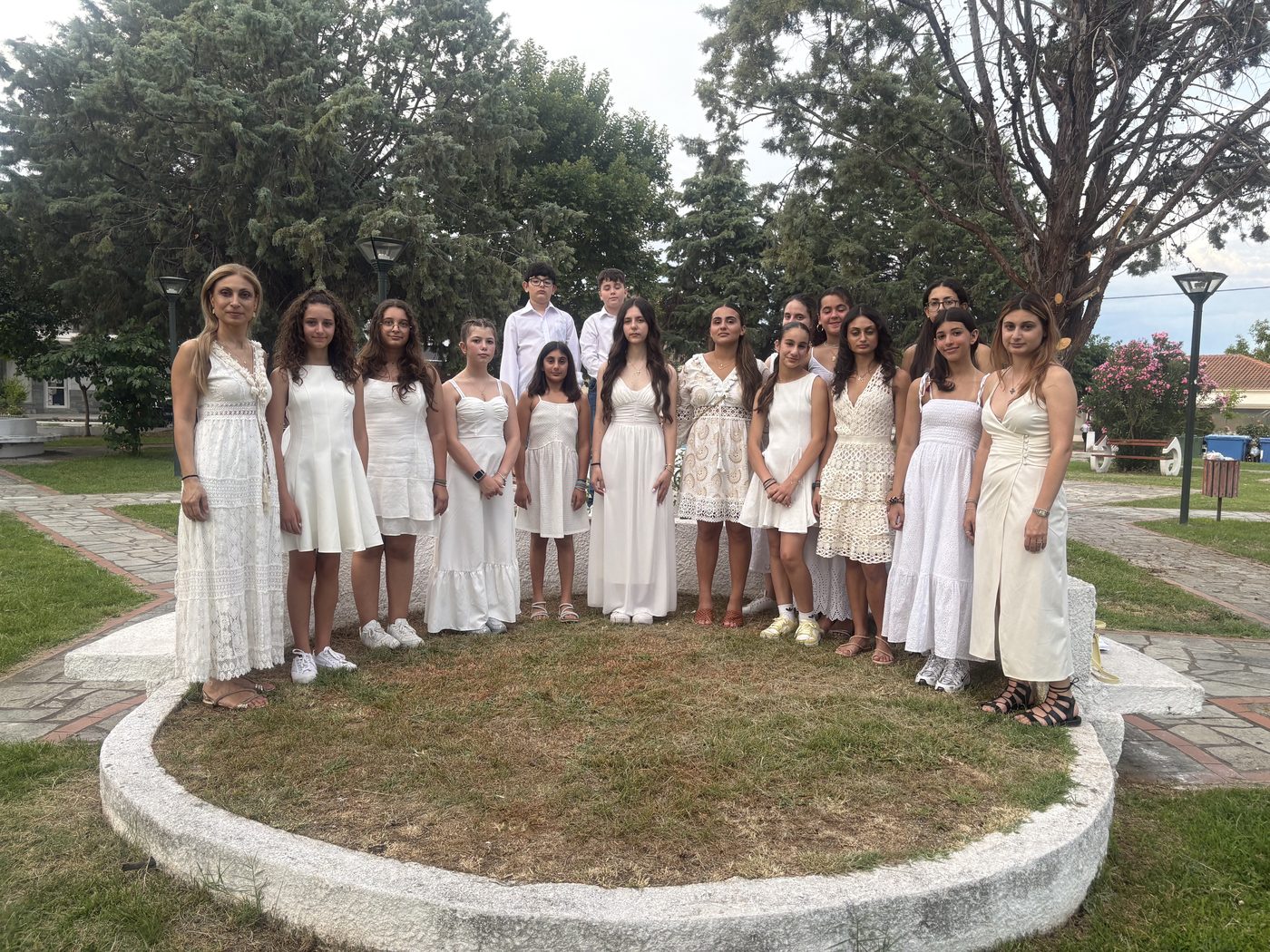 Choir members in white outfits posing outdoors among trees