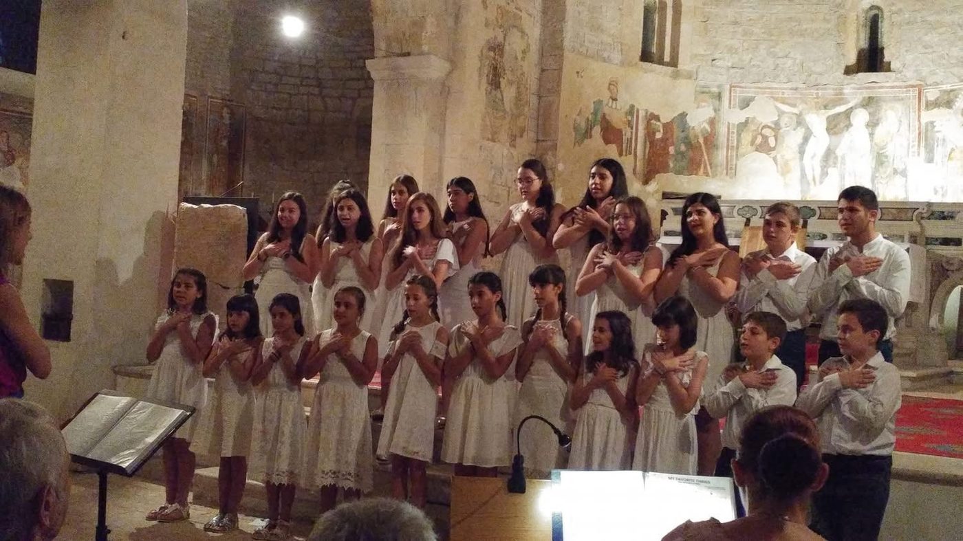 Teenage choir members performing inside a frescoed church with hands over their hearts