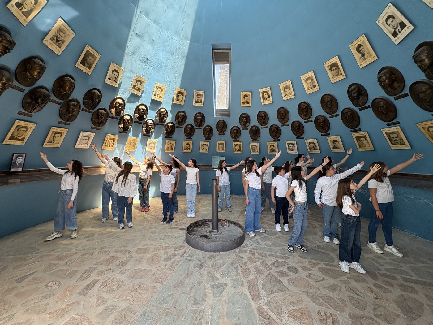 Group of young people with arms raised inside a memorial hall lined with portraits