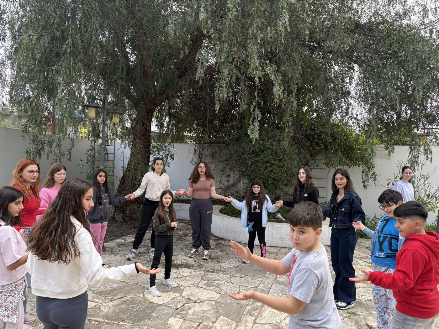 Group of young people playing a circle game outdoors under a tree