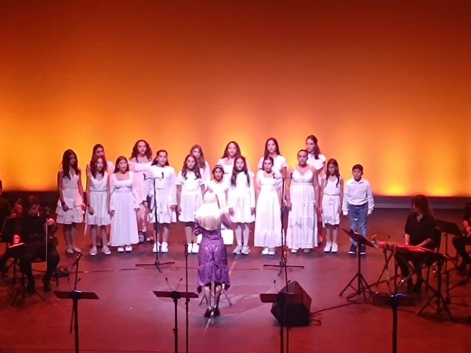 Youth choir in white dresses performing under warm orange stage lighting